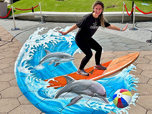 Posing with 3D chalk art of surfboard, dolphins and beach ball.