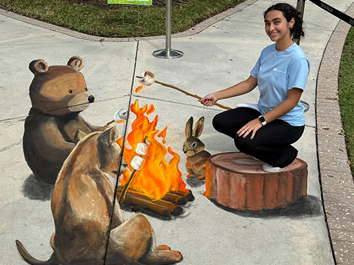 Posing with 3D chalk art of forest animals toasting marshmallows around a fire