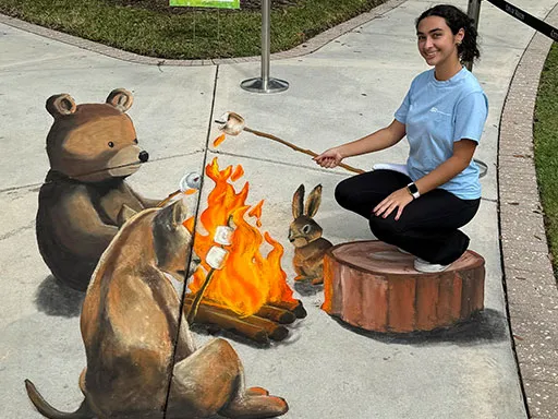 Posing with 3D chalk art of forest animals toasting marshmallows around a fire