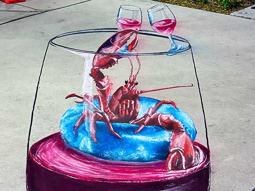 3D chalk art of lobster floating on pool floatie inside a wine glass