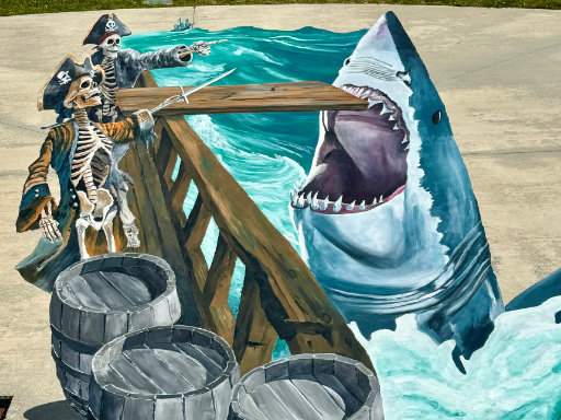 3D painted vinyl image of a ghost ship with skeletons pointing toward the plank and a leaping shark with open mouth.