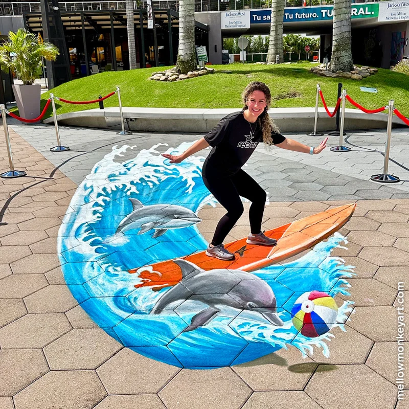 Posing with 3D chalk art of surfboard, dolphins and beach ball.