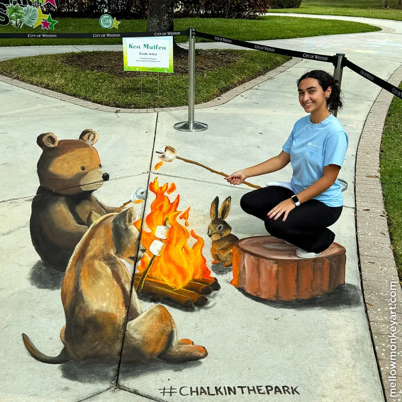 Posing with 3D chalk art of forest animals toasting marshmallows around a fire