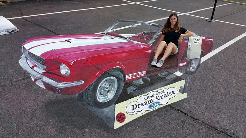 3D chalk art of girl sitting in a kiddie ride shaped like an antique Ford Mustang